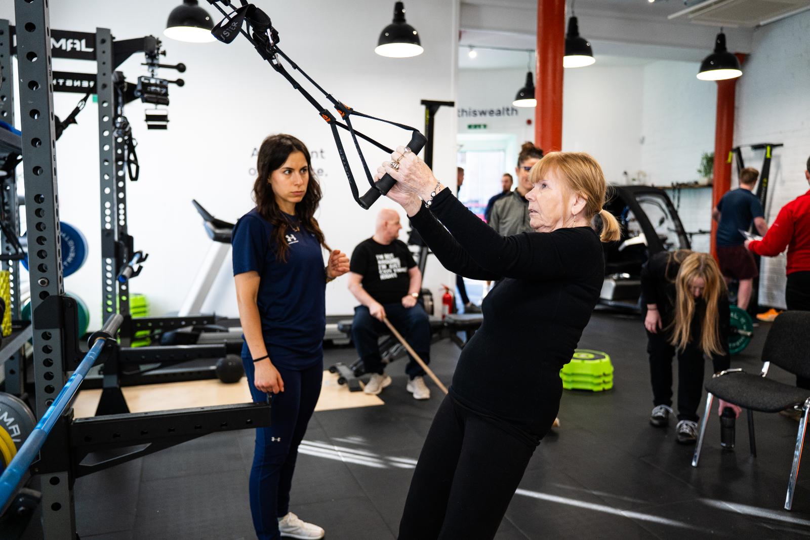 KA3_2543 A woman performing a guided suspension trainer (TRX) exercise under the supervision of a rehab coach.