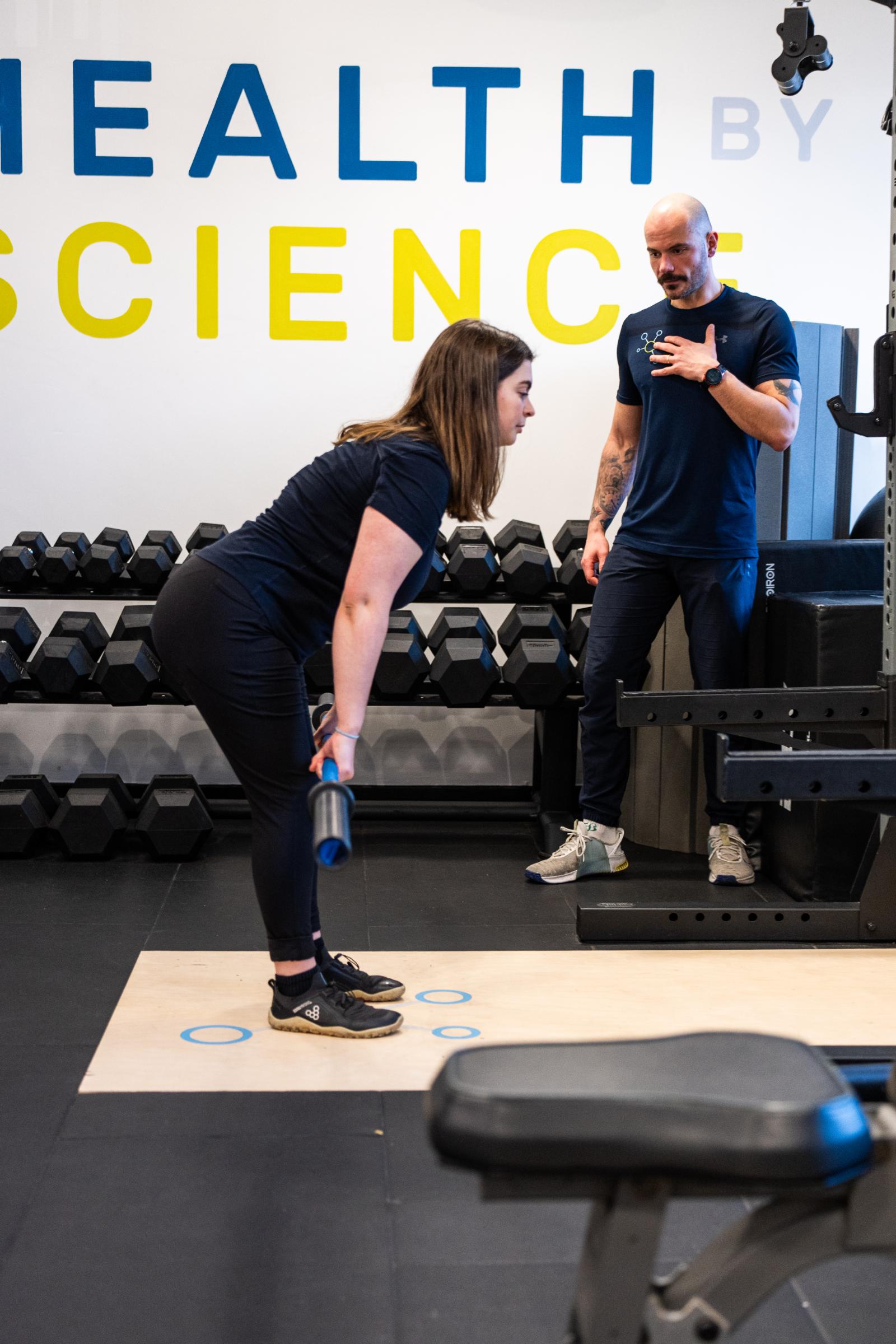 KA3_2894 Health by Science specialist providing clinical cues for a barbell Romanian deadlift to assess posterior chain engagement.