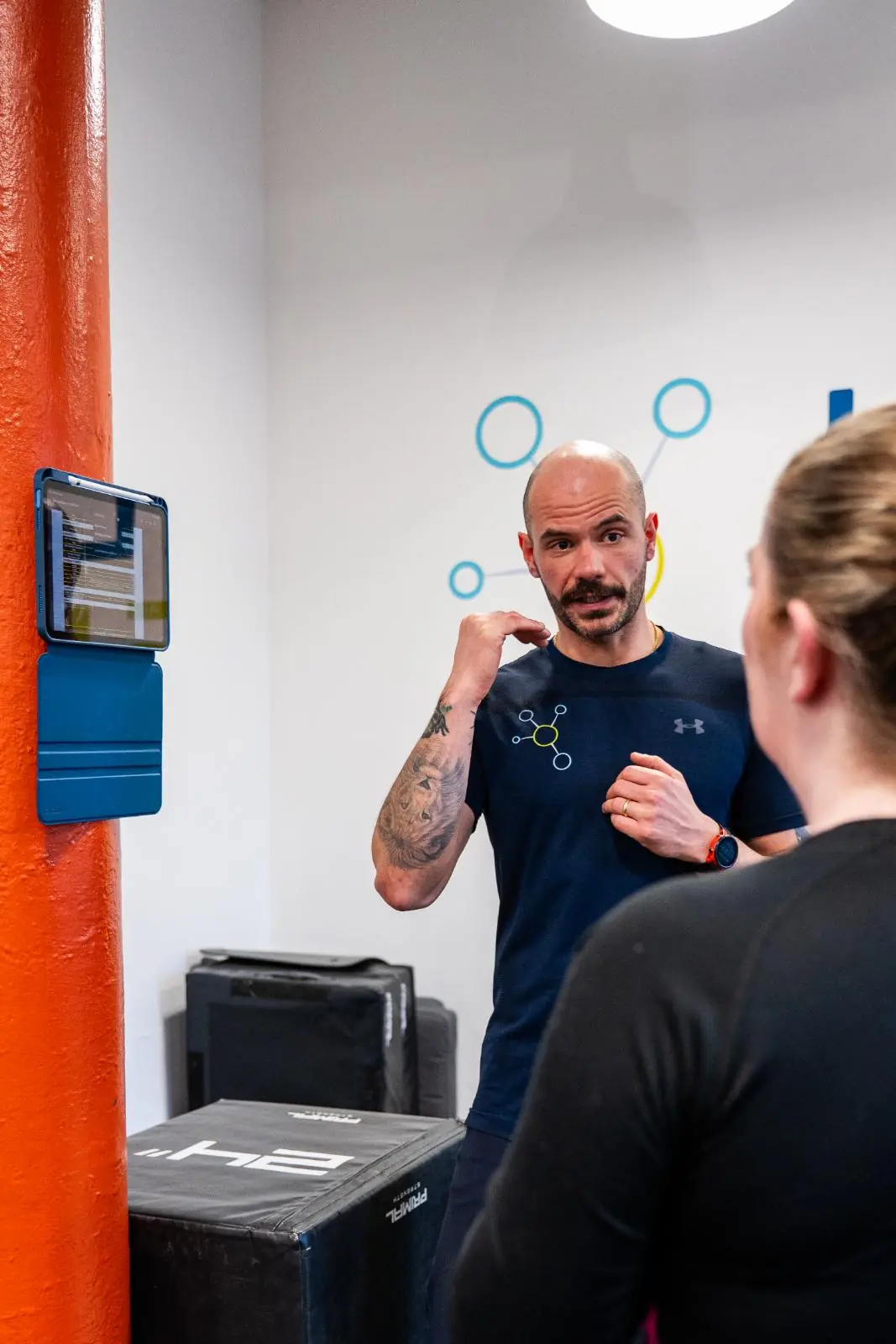 KA3_2974 Practitioner explaining movement mechanics and rehabilitation progress using a wall-mounted tablet interface.