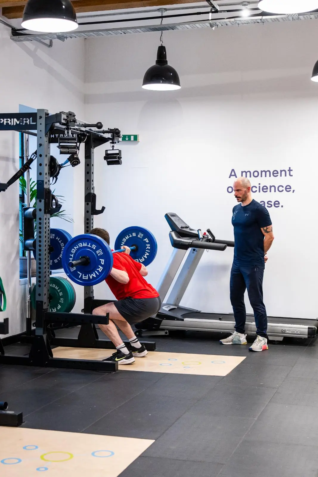 KA3_3114 Clinical specialist monitoring barbell squat depth and spinal alignment for a personal training Edinburgh client.