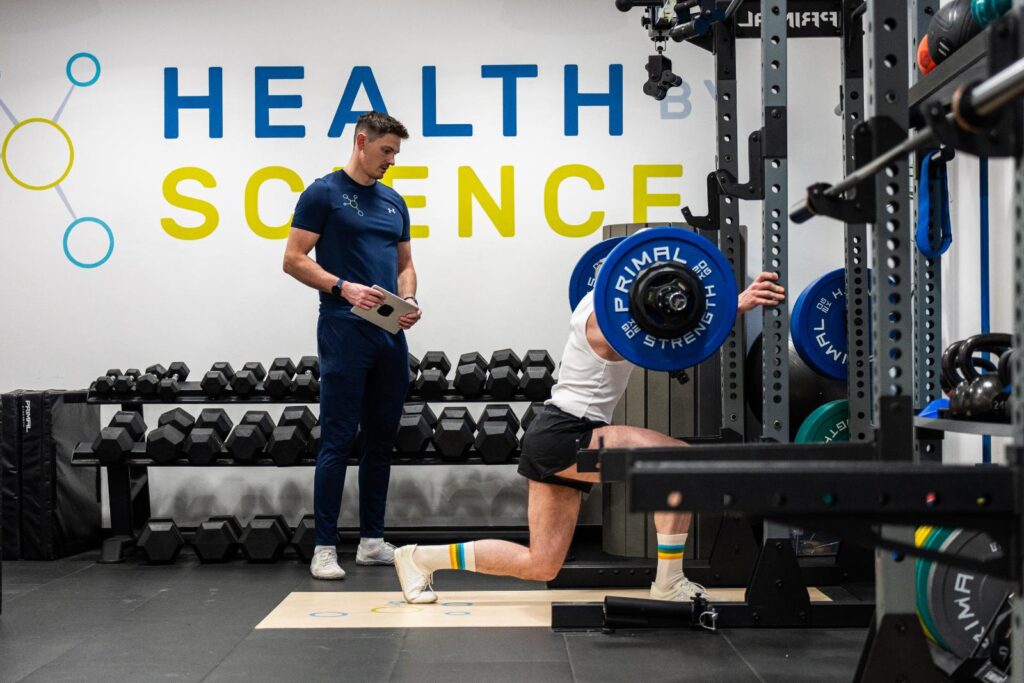 A Health by Science coach watching a client's barbell split squat to assess leg strength and knee stability