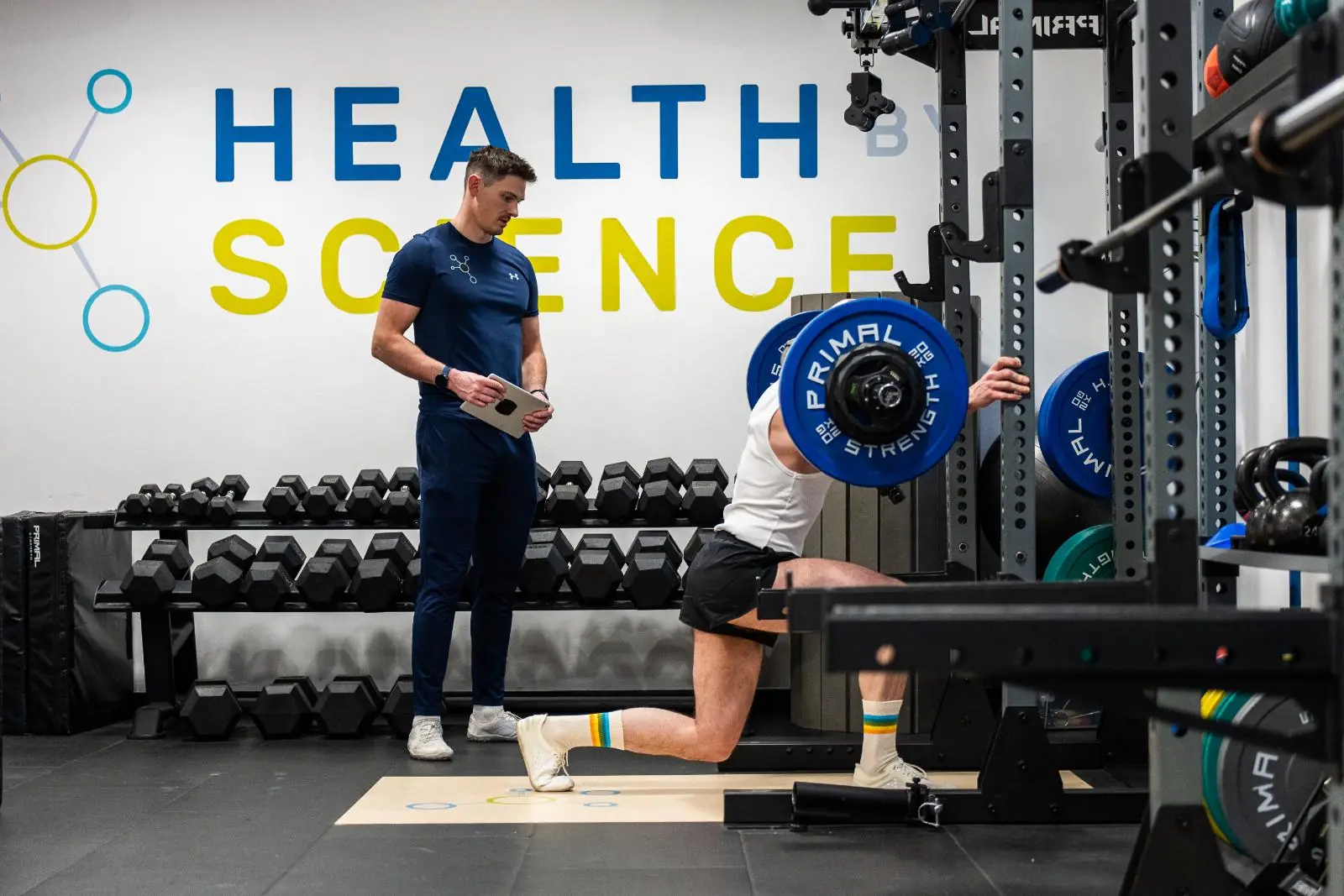 Health by Science coach monitoring a barbell split squat to assess unilateral leg strength and knee stability.