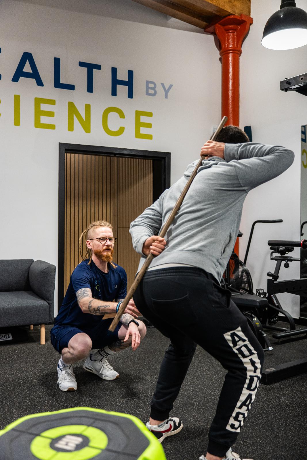 KA3_3820 Specialist conducting a biomechanical assessment using a dowel to analyse hip hinge and spinal alignment in our Leith clinic.