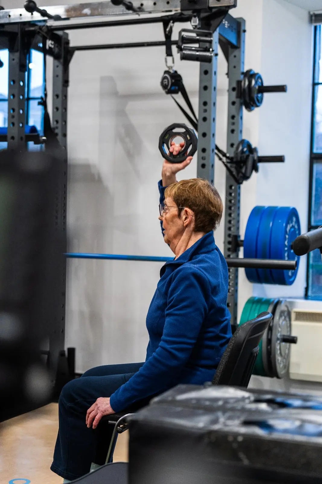 KA3_3902 Specialist monitoring a seated single-arm overhead press for an older adult to assess upper body strength and joint health.