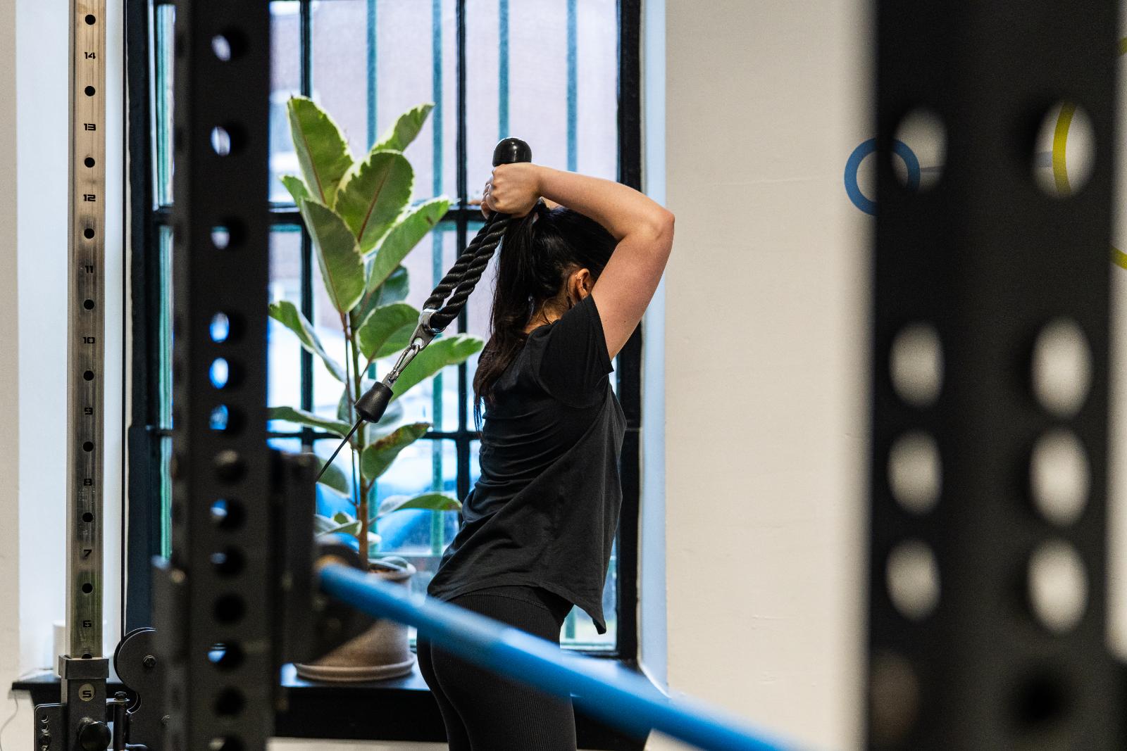 KA3_4174 Client performing a cable overhead triceps extension under clinical supervision to improve upper body strength and joint stability.