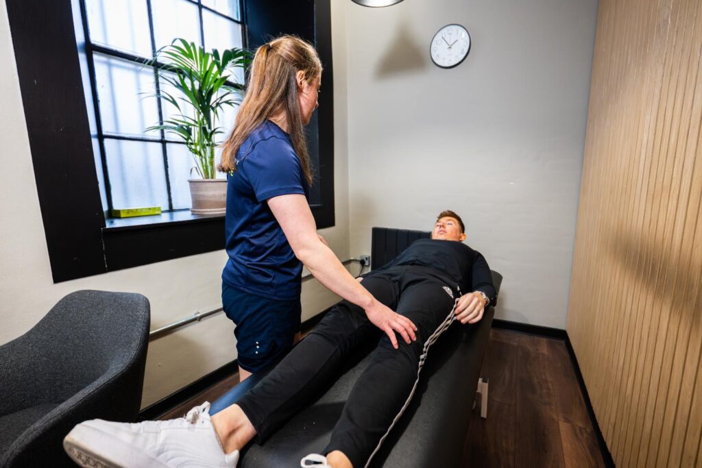 A Health by Science clinician assessing a patient’s leg on the treatment table in the Leith clinic