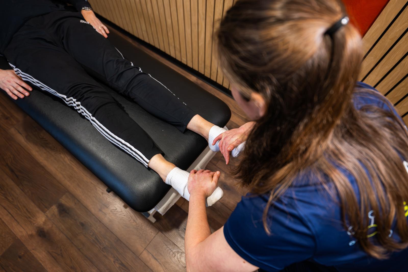 Overhead view of a specialist conducting a manual clinical assessment of bilateral ankle mobility to identify muscular imbalances.