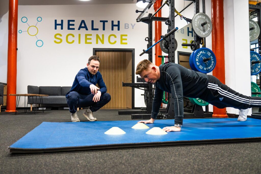 A Health by Science clinician coaching a strength exercise on the gym floor as part of an active rehabilitation plan