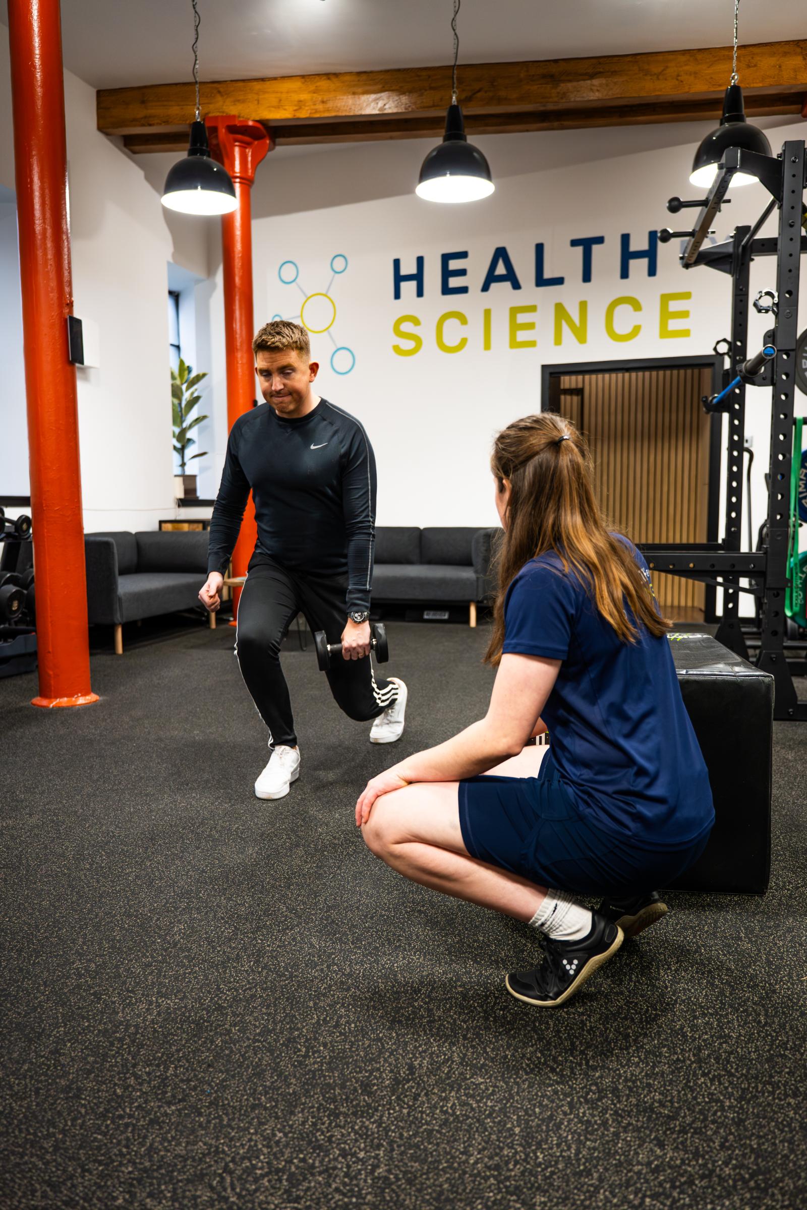 KA3_5221 Health by Science specialist monitoring a weighted reverse lunge to assess lower body stability and unilateral strength for a rehabilitation patient.